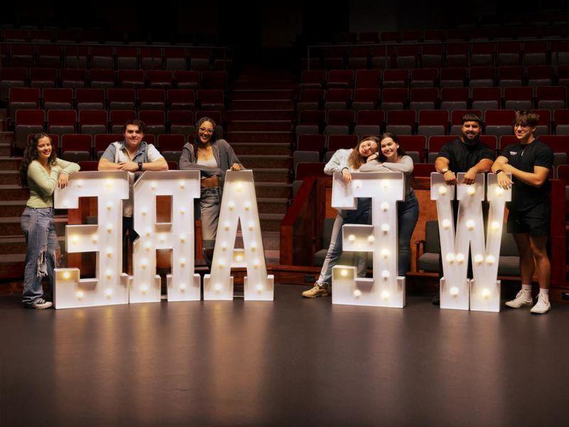 New Kensington students standing behind large letters that spell "WE ARE" inside the campus theatre.